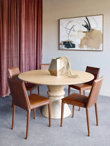 Round wooden dining table with pedestal base in elegant dining room setting.