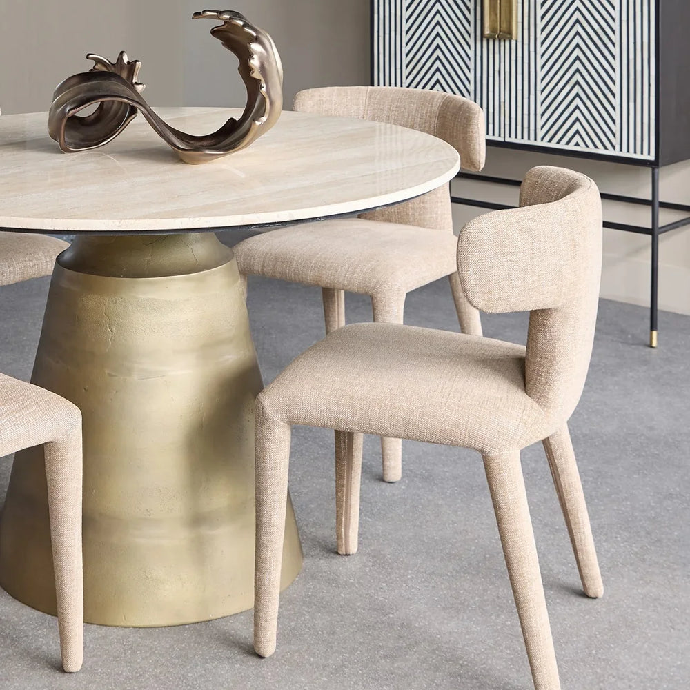 Wheat-colored dining chairs around a round table with a brass base in a modern dining room.