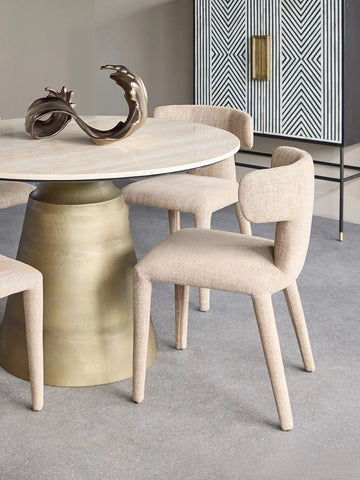 Wheat-colored dining chairs around a round table with a brass base in a modern dining room.