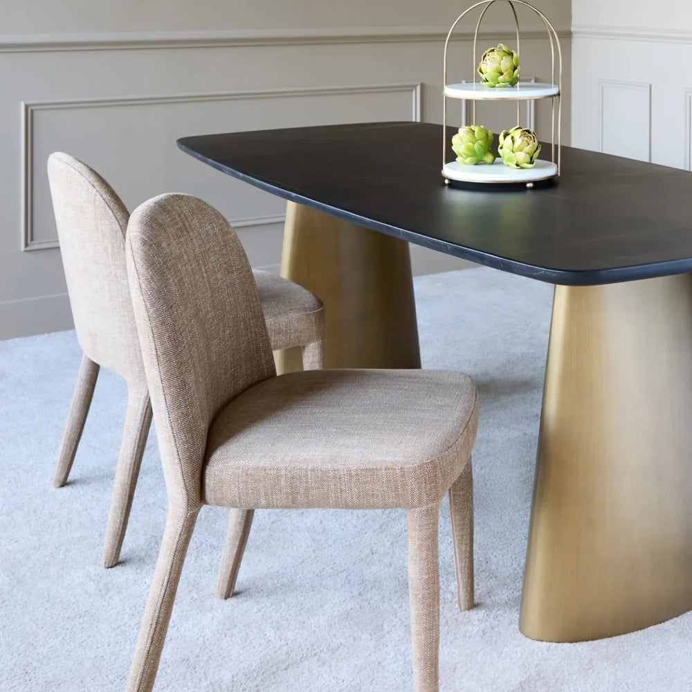 Wheat upholstered dining chairs beside a dark table with gold legs in a modern room.