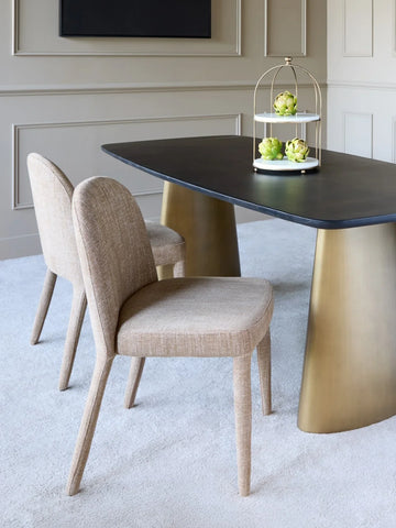Wheat upholstered dining chairs beside a dark table with gold legs in a modern room.