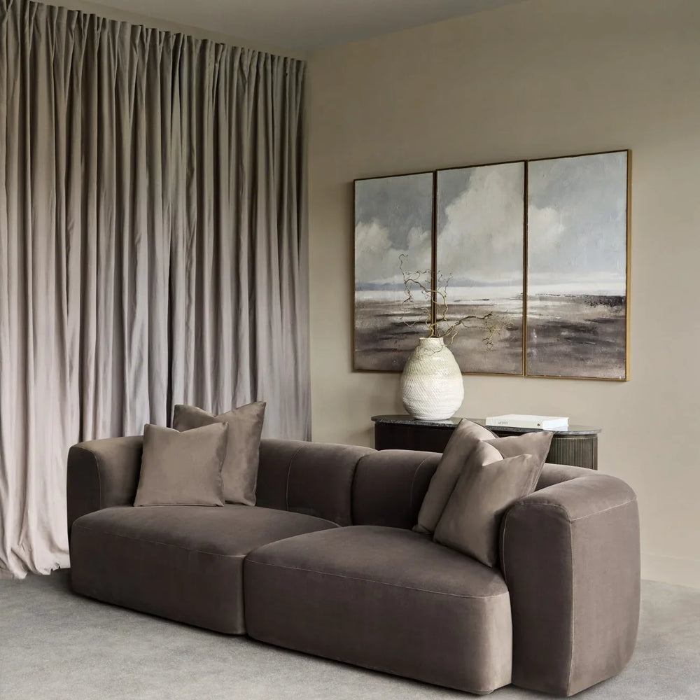 Brown velvet sofa in a modern living room with abstract art and soft drapes.