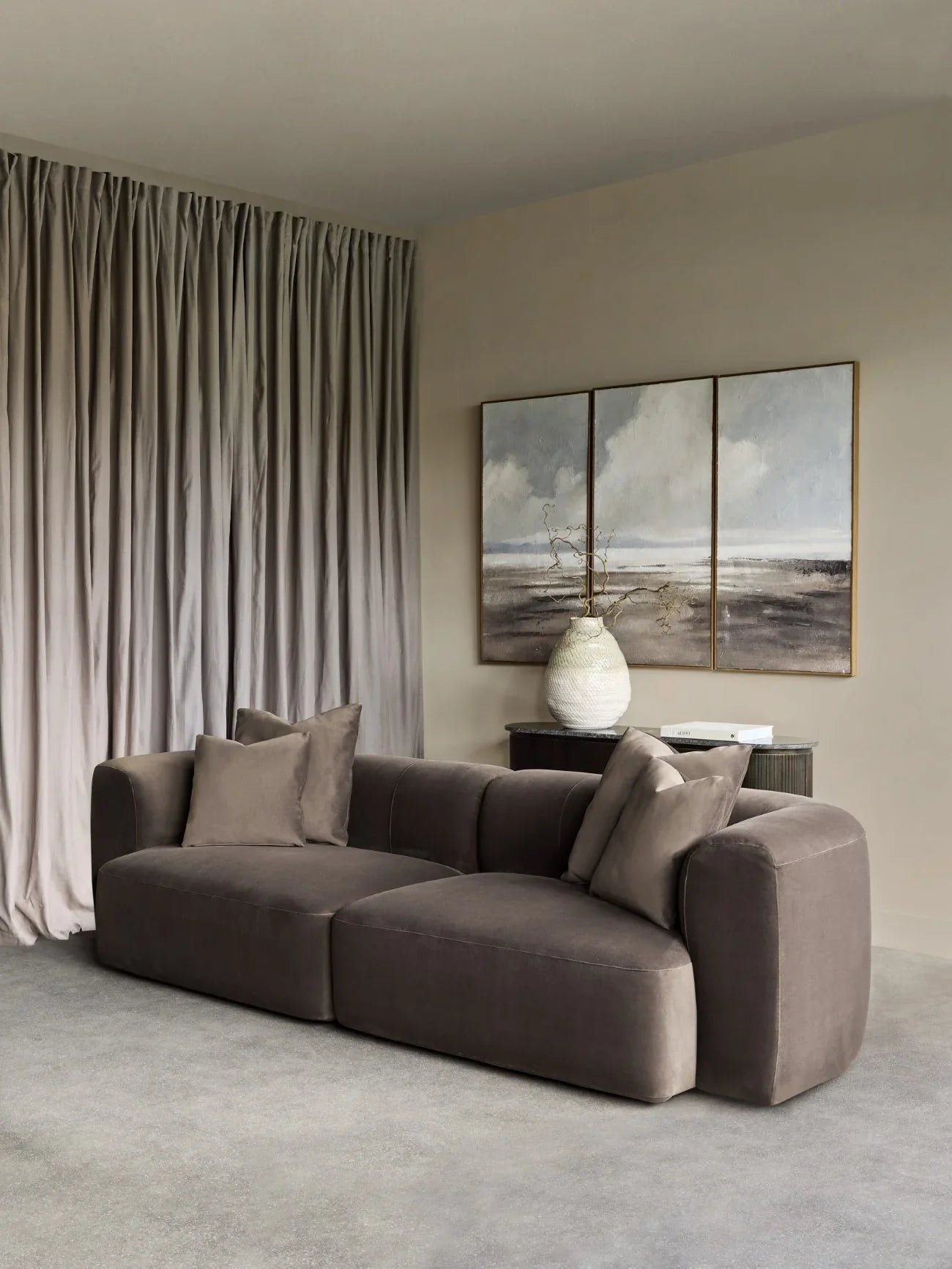 Brown velvet sofa in a modern living room with abstract art and soft drapes.