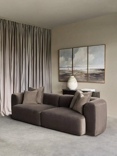 Brown velvet sofa in a modern living room with abstract art and soft drapes.