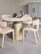 Beige dining chairs around a round travertine table with a bronze sculpture centerpiece.