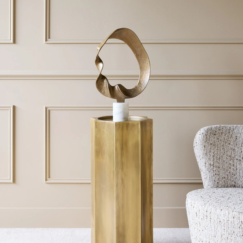 Antique brass pedestal with abstract sculpture in elegant living room setting.