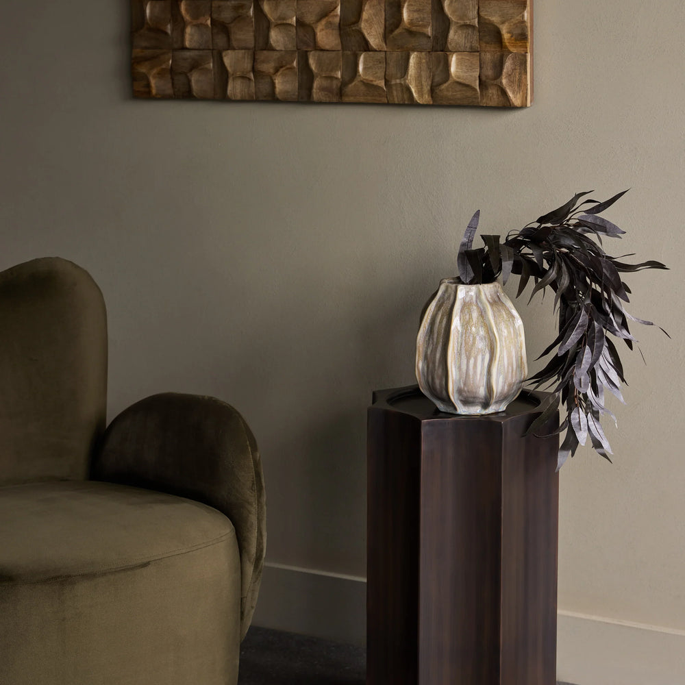 Bronze pedestal with vase and foliage in elegant living room setting.