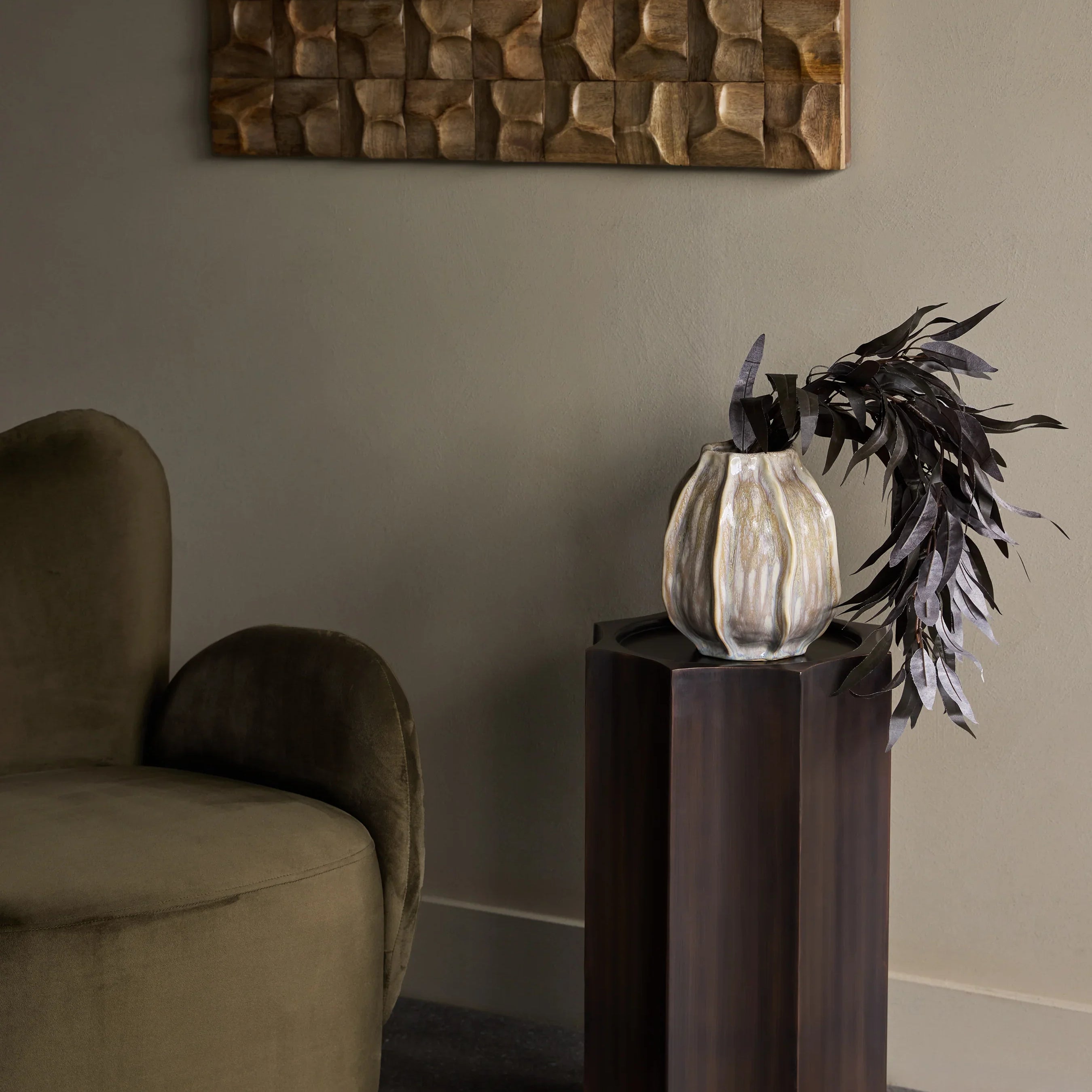 Bronze pedestal with vase and foliage in elegant living room setting.