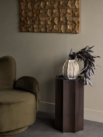 Bronze pedestal with vase and foliage in elegant living room setting.