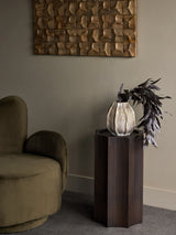 Bronze pedestal with vase and foliage in elegant living room setting.