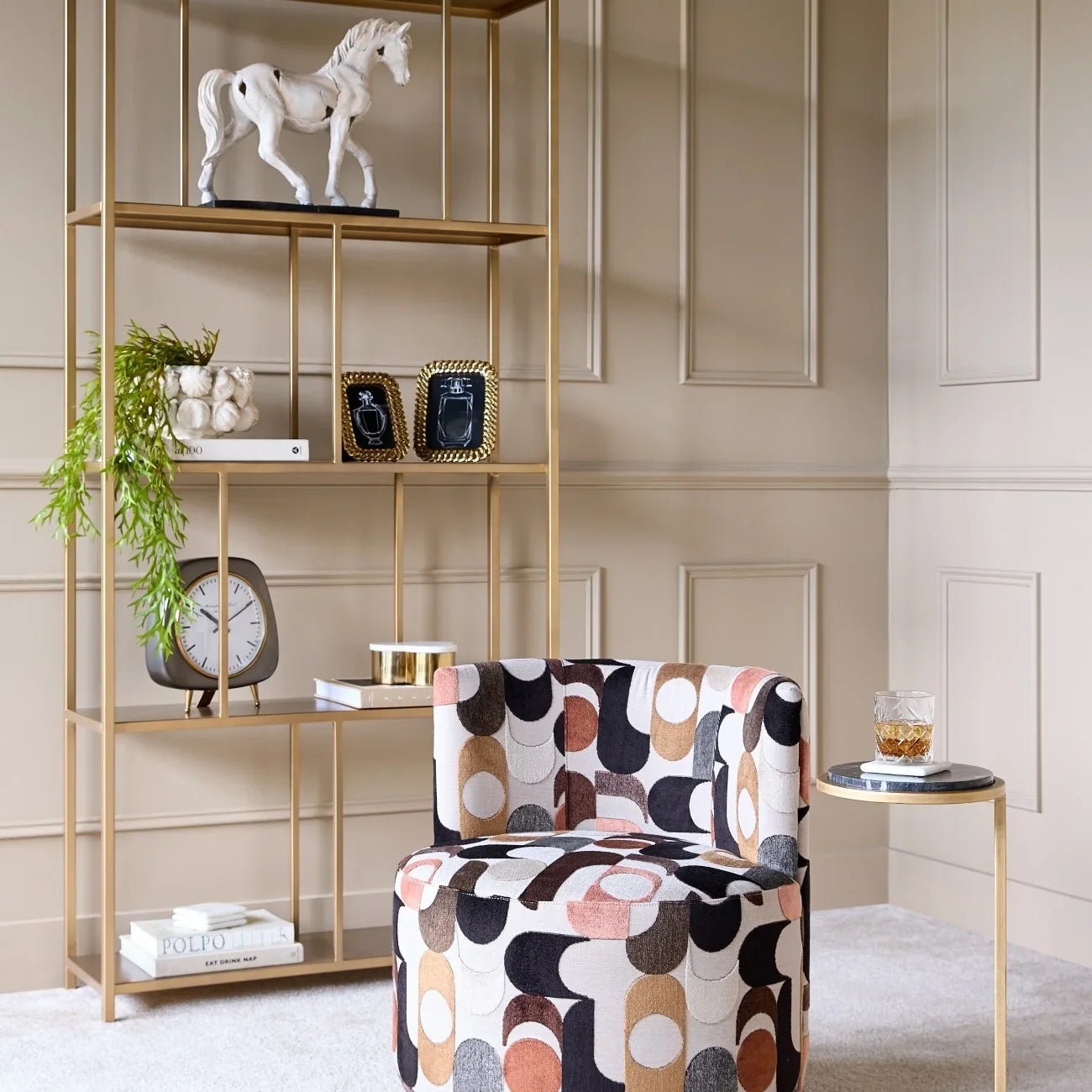 Black marble side table with gold frame beside patterned chair in elegant room.