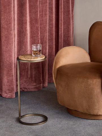 Marble-topped side table with gold frame beside a plush brown chair and pink curtains.