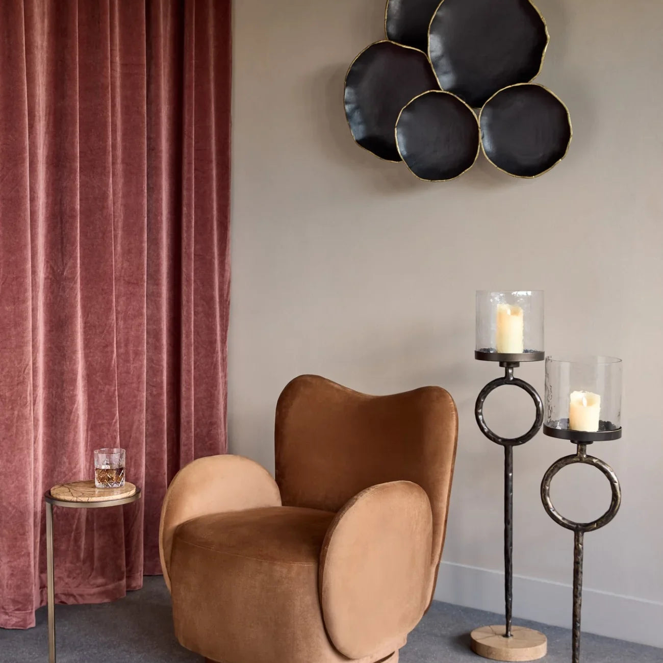 Brown marble side table beside plush chair and tall candle holders in elegant room.