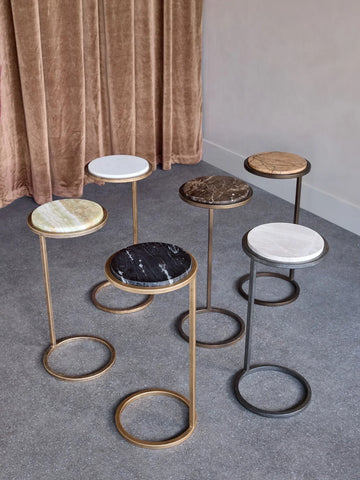 Assorted marble-topped accent tables with gold and bronze frames on a grey floor.