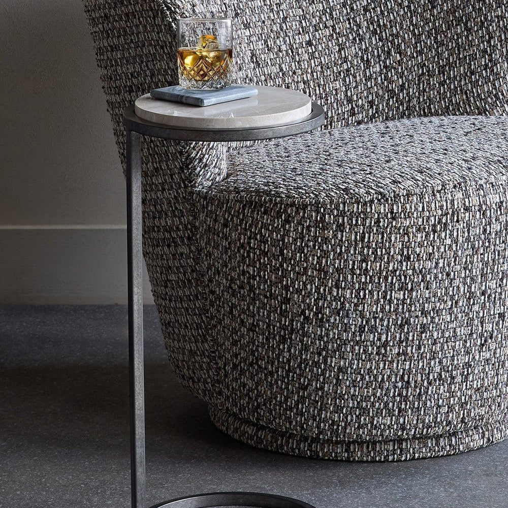 Grey marble side table beside textured armchair with a drink on top.