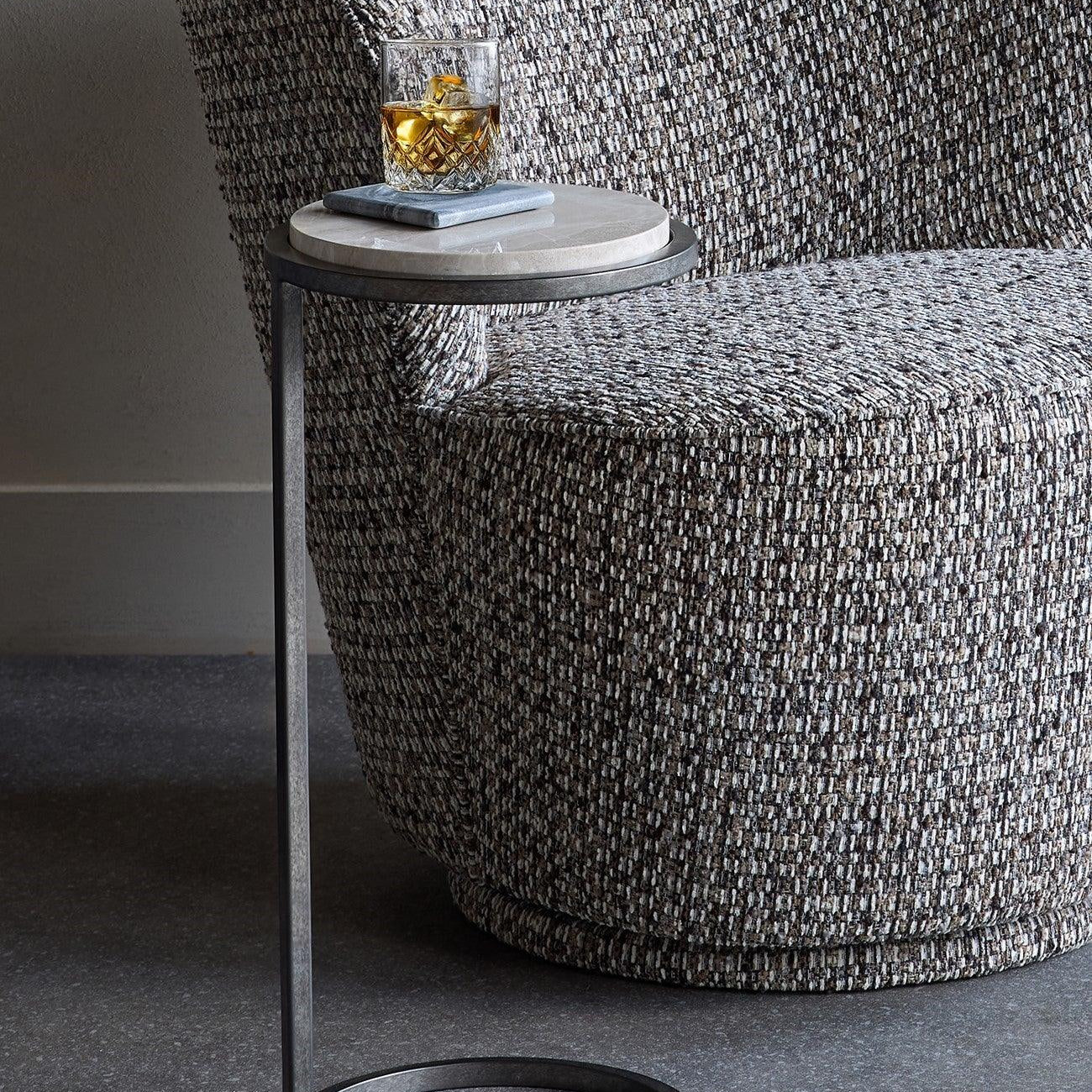 Grey marble side table beside textured armchair with a drink on top.