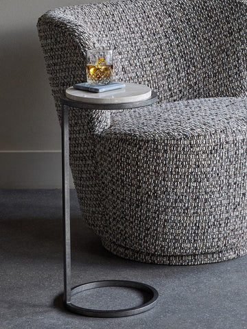 Grey marble side table beside textured armchair with a drink on top.