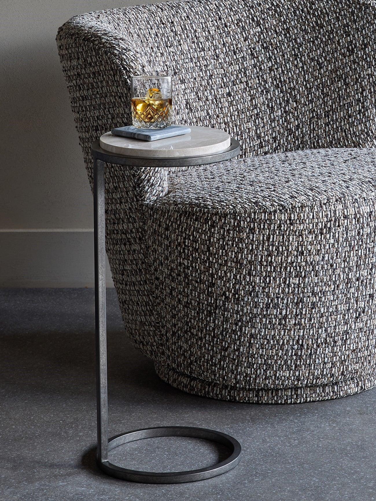 Grey marble side table beside textured armchair with a drink on top.