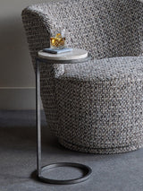 Grey marble side table beside textured armchair with a drink on top.