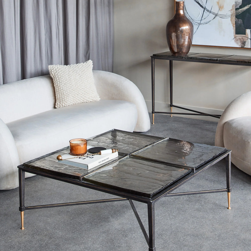 Glass coffee table in modern living room with white sofas and abstract art.