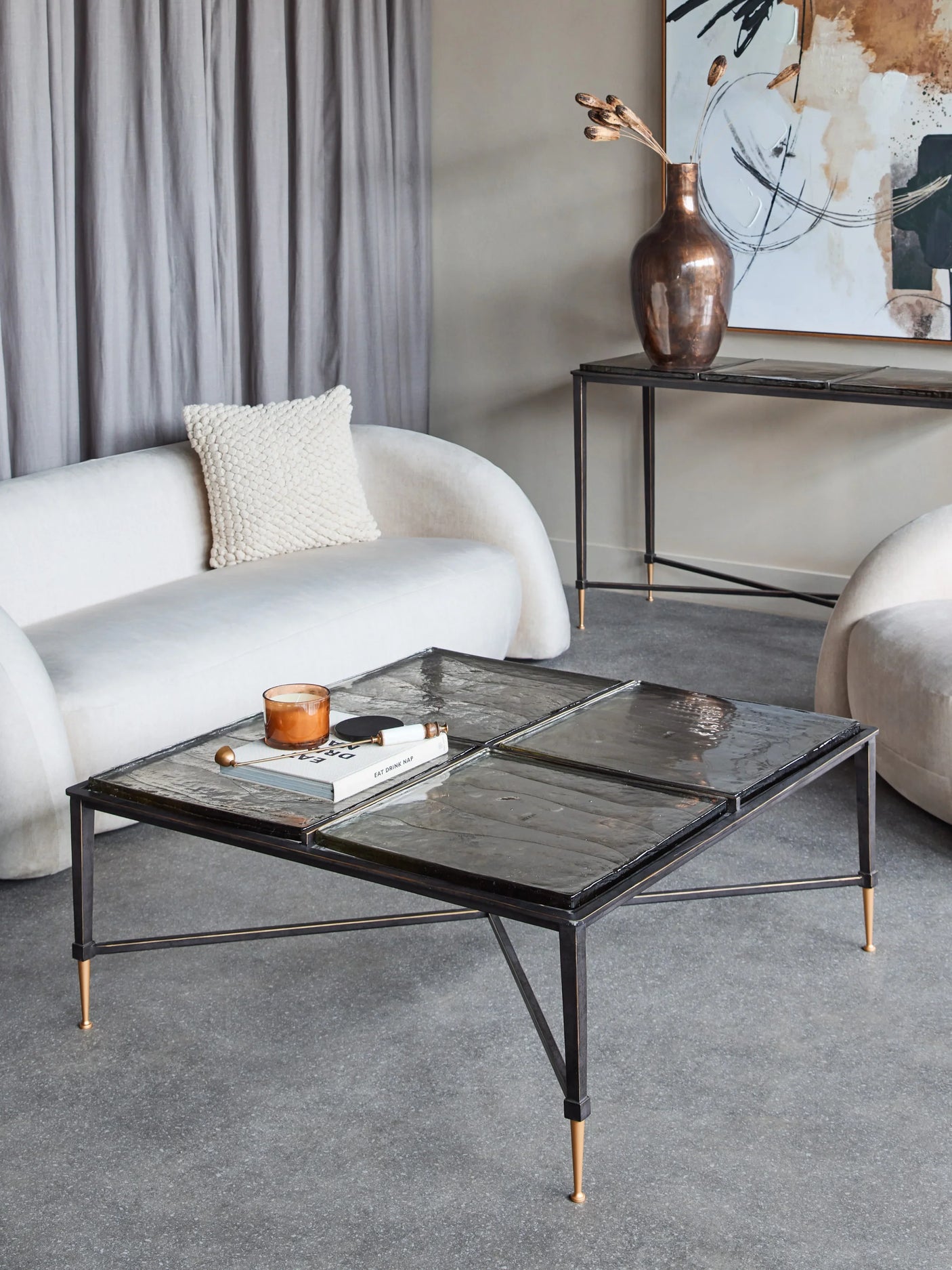 Glass coffee table in modern living room with white sofas and abstract art.