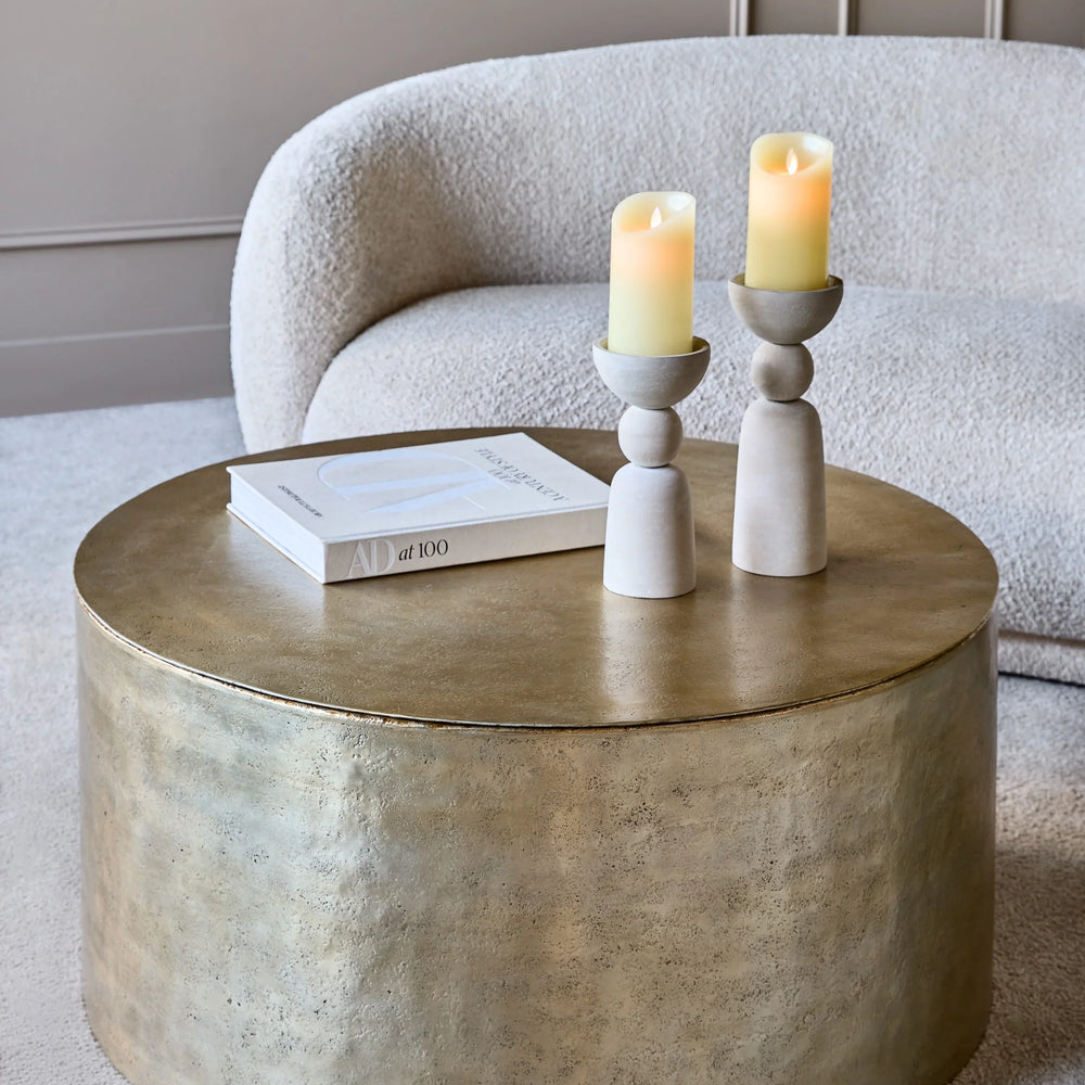 Gold metal drum coffee table with candles and book in cozy living room.