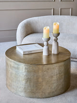 Gold metal drum coffee table with candles and book in cozy living room.