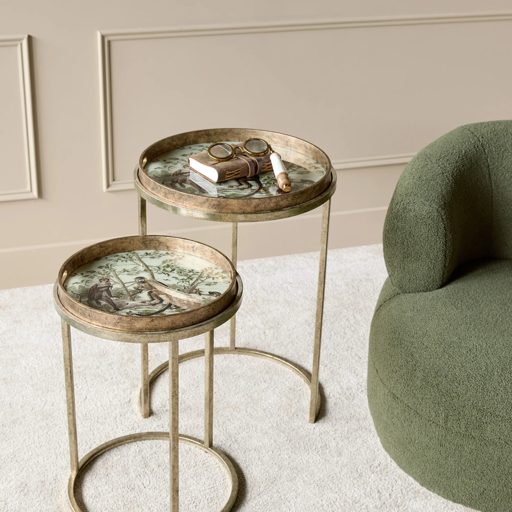Golden side tables with jungle design, styled next to a green chair on beige carpet.