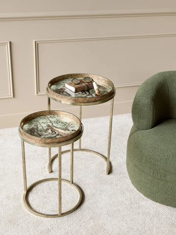 Golden side tables with jungle design, styled next to a green chair on beige carpet.