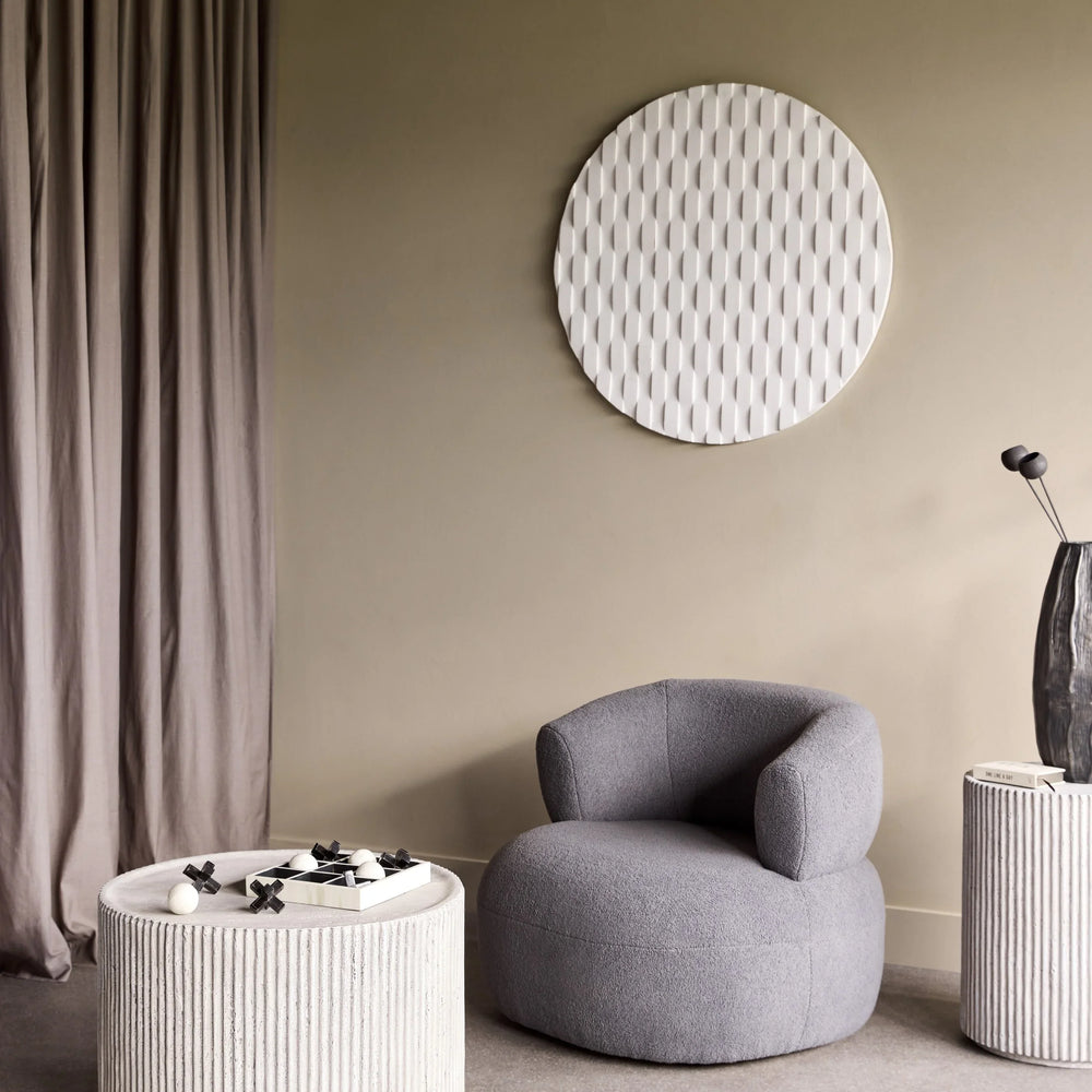 Beige ribbed coffee table with decor, next to a grey armchair in a modern room.