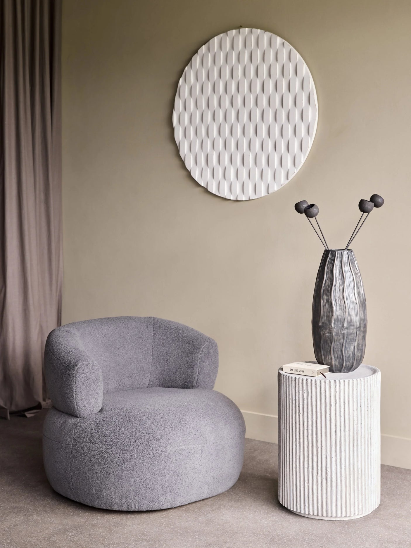 Grey side table with ribbed texture beside a cozy armchair in a modern living room.