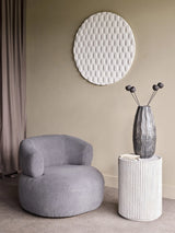 Grey side table with ribbed texture beside a cozy armchair in a modern living room.