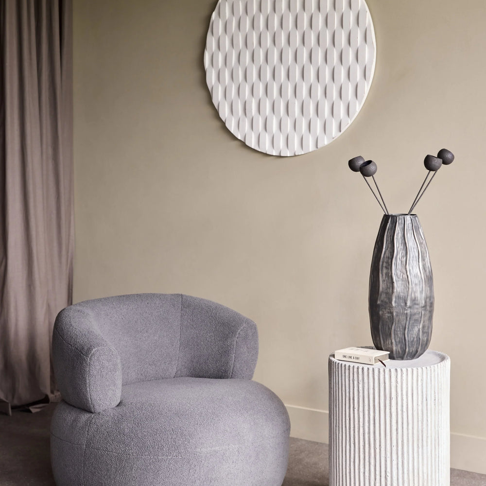 Textured white side table with vase beside a grey armchair in a modern living room.