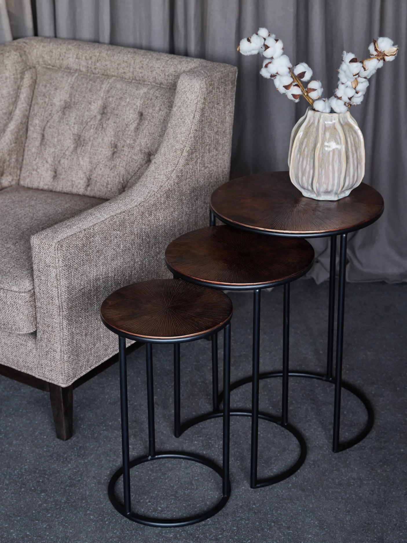 Dark wood and metal nesting tables beside a textured beige armchair.