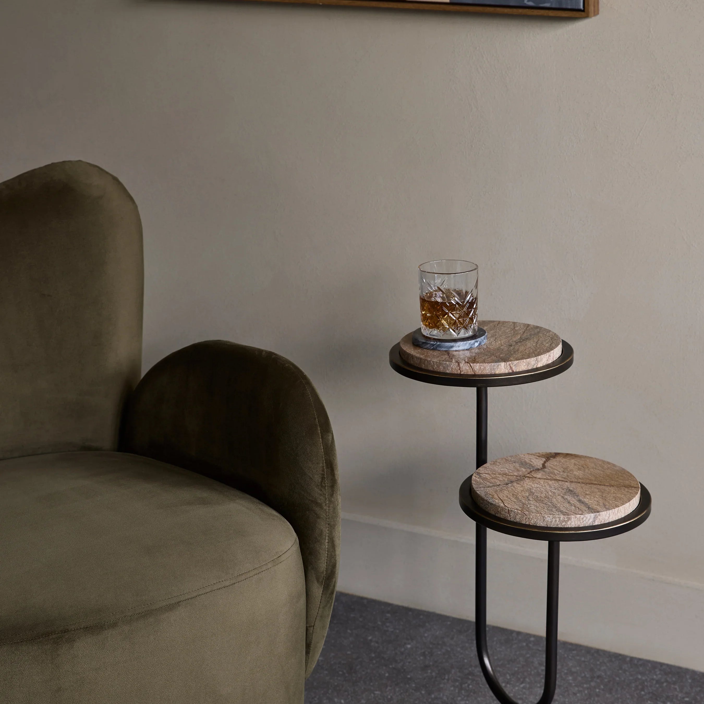 Two-tiered brown accent table beside a green velvet chair.