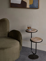 Two-tiered brown accent table beside a green velvet chair.