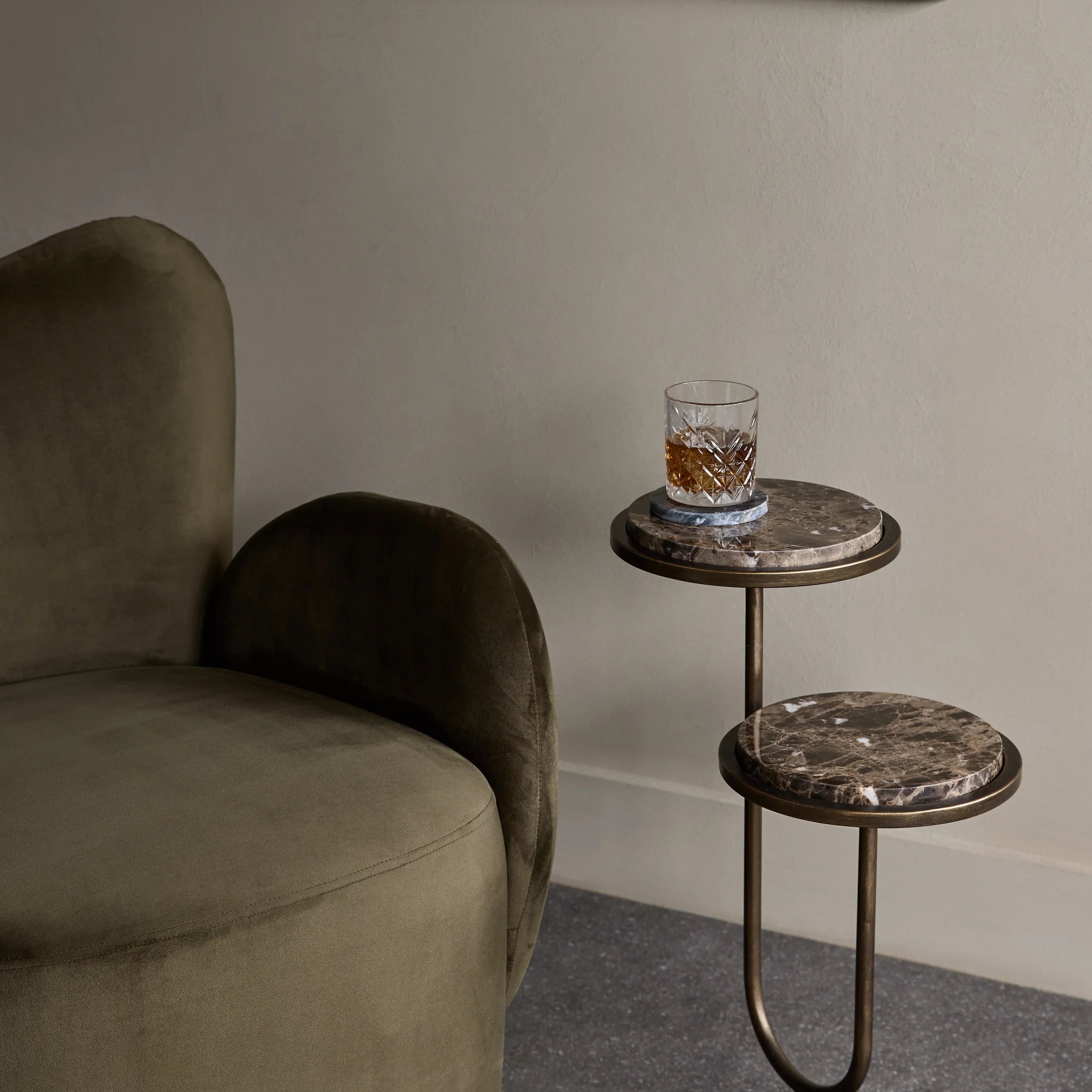 Dark marble accent table beside olive green chair in modern living room.