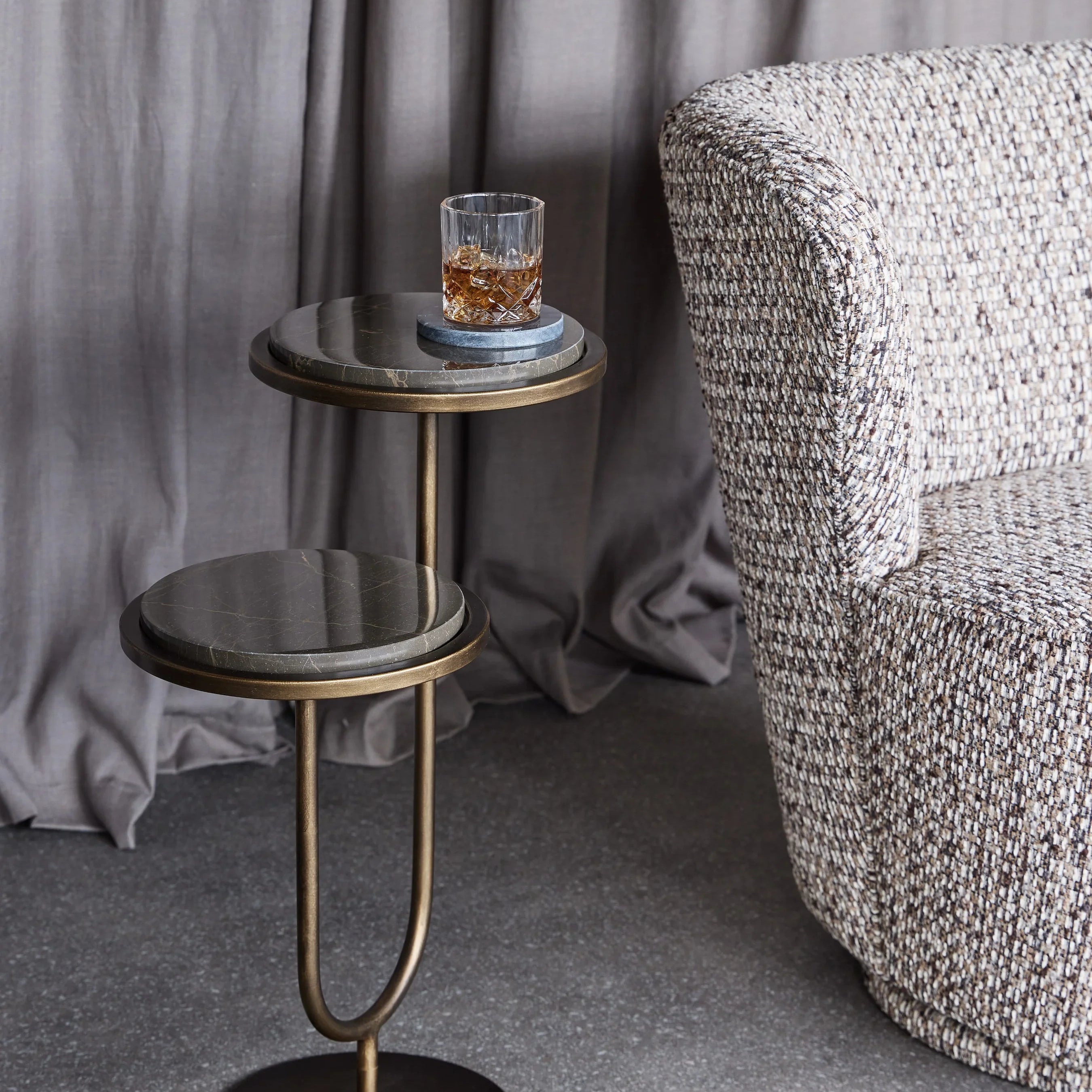 Gold marble accent table with a drink, next to a textured armchair.