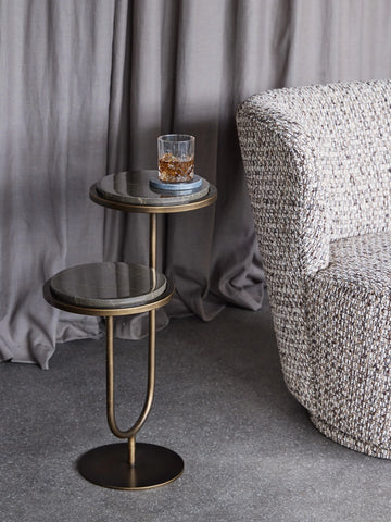 Gold marble accent table with a drink, next to a textured armchair.