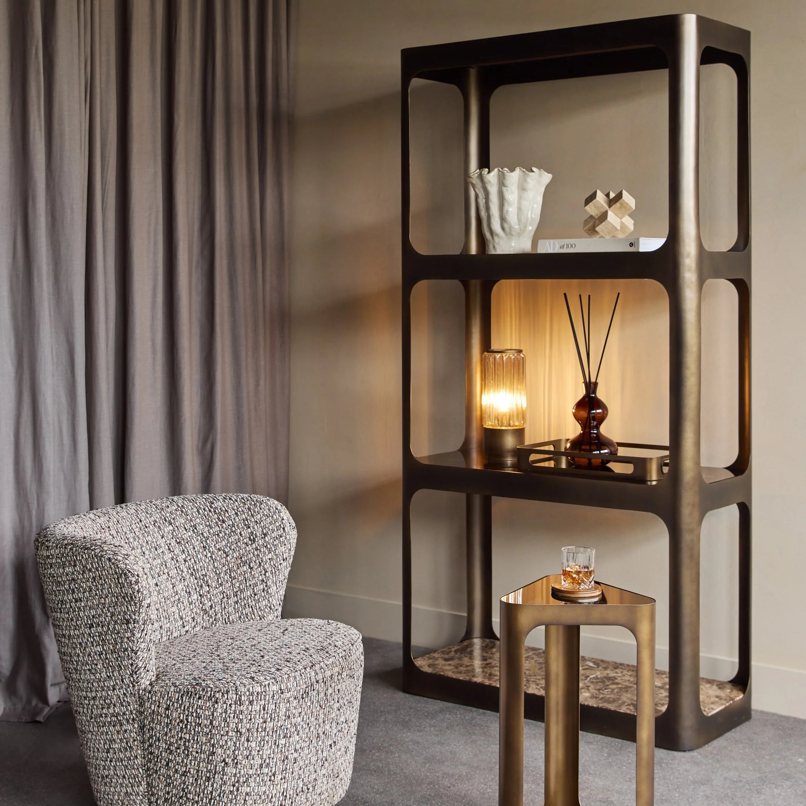 Triangular glass accent table in modern living room with armchair and shelf.