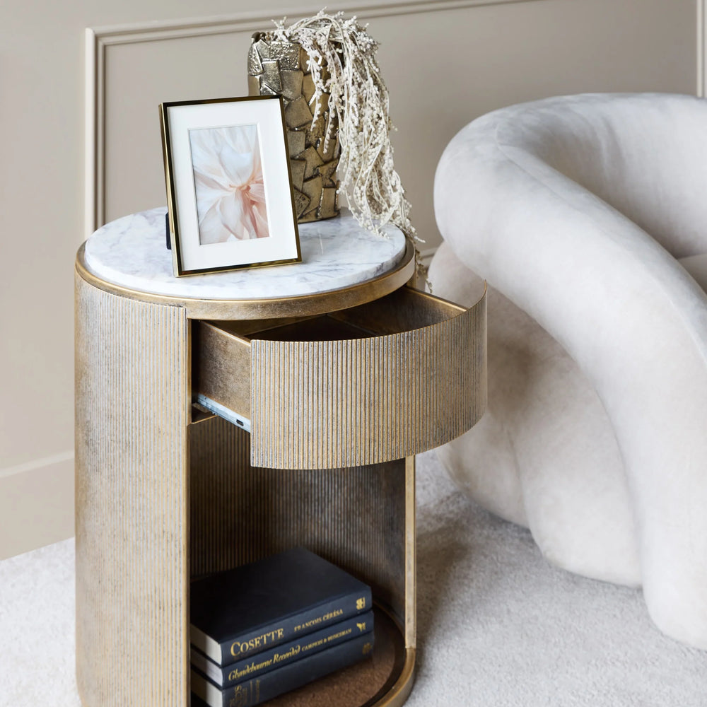 Aged gold bedside table with marble top, drawer open, and books on lower shelf.