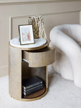 Aged gold bedside table with marble top, drawer open, and books on lower shelf.