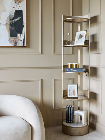 Aged gold round shelving unit in a beige room with books and decorative items.