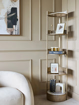 Aged gold round shelving unit in a beige room with books and decorative items.