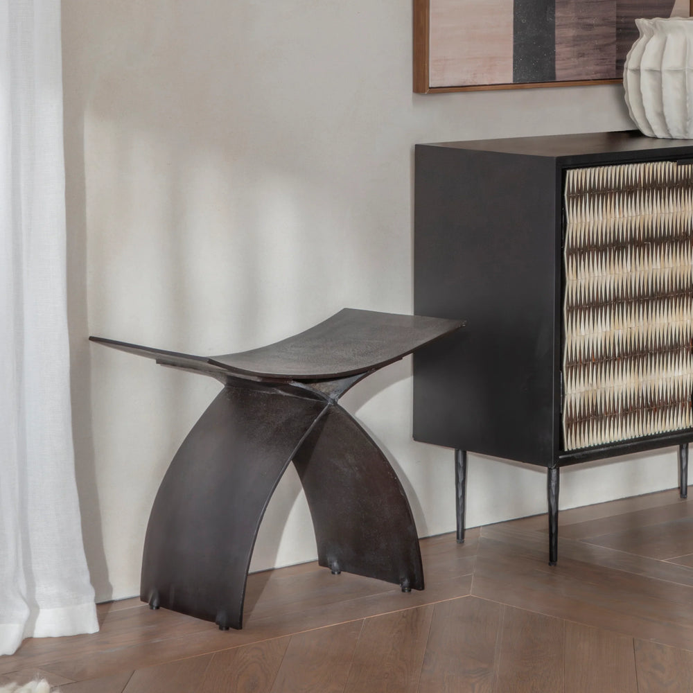 Dark iron stool in a modern room with wooden flooring and abstract artwork.