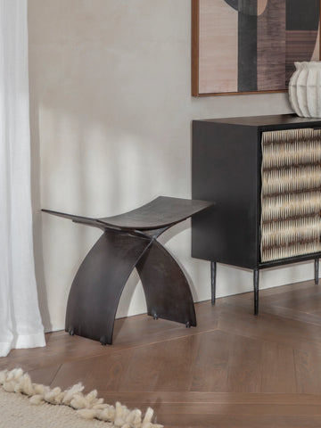 Dark iron stool in a modern room with wooden flooring and abstract artwork.