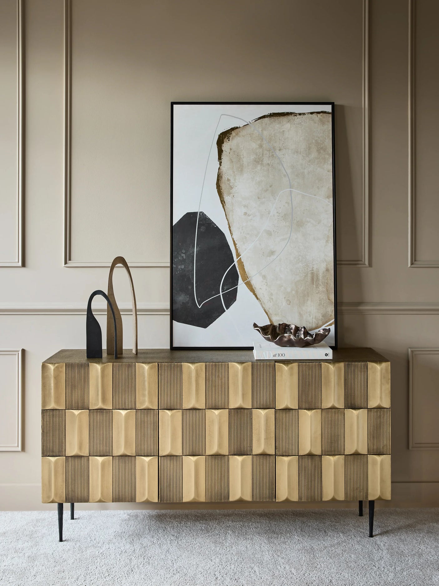 Brass sideboard with textured front, styled with abstract art and decor.