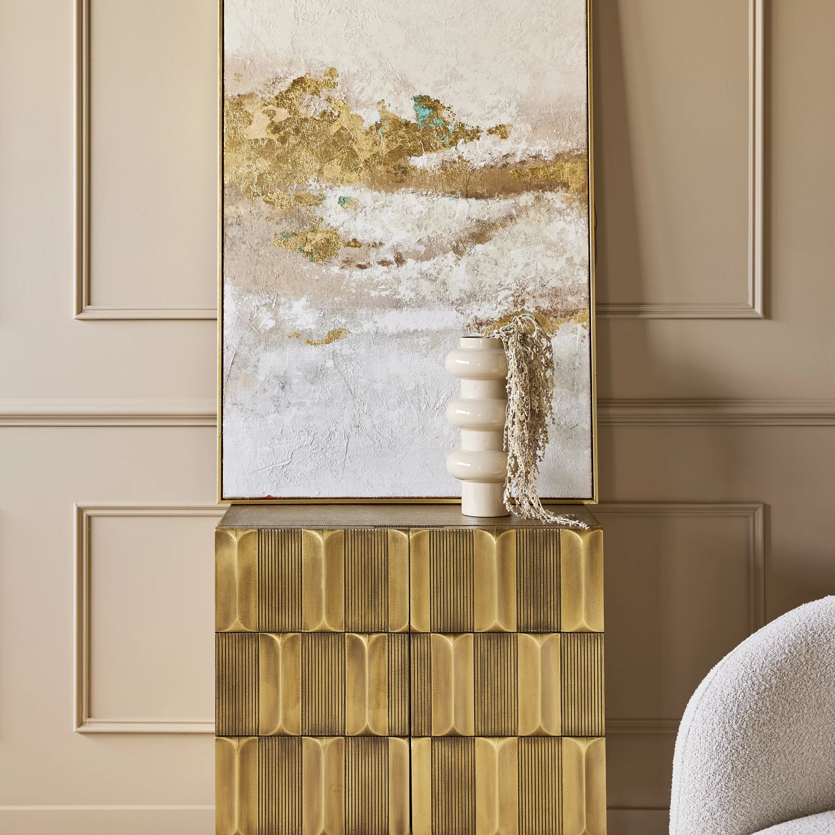 Gold-toned cabinet in elegant room with abstract art and vase.