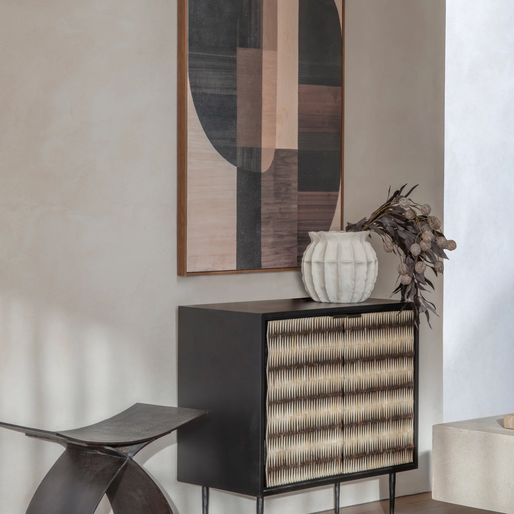 Black cabinet with patterned doors in modern room, abstract art above.