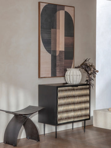 Black cabinet with patterned doors in modern room, abstract art above.
